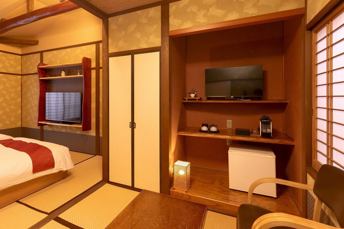 Ein traditioneller japanischer Raum mit Tatami-Bodenbelag, einem Bett, einem Fernseher und einem kleinen Kühlschrank.