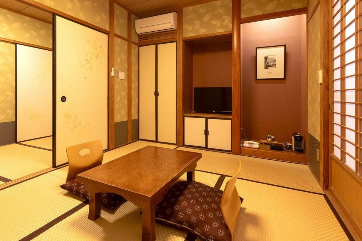 A traditional Japanese room with tatami flooring, a wooden table, chairs, a television, and a sliding door.