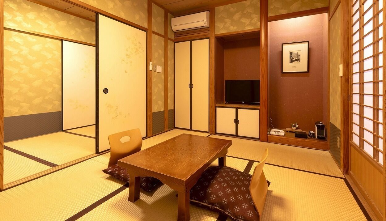 Perinteinen japanilainen huone, jossa on tatamimatto, puinen pöytä, tuoleja, televisio ja liukuovi.