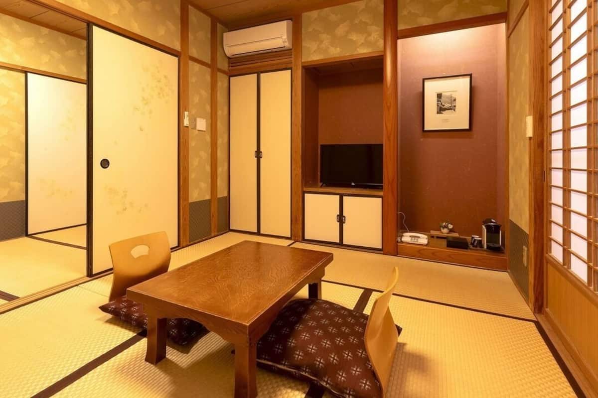 Ett traditionellt japanskt rum med tatamimattor på golvet, ett träbord, stolar, en tv och en skjutdörr.
