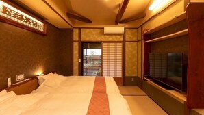 A traditional Japanese-style bedroom with tatami flooring, a large bed, a television, and a sliding door leading to a balcony.