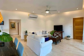Ein Wohnzimmer mit einem weißen Sofa, einem Couchtisch, einem Fernseher und einem Deckenventilator.