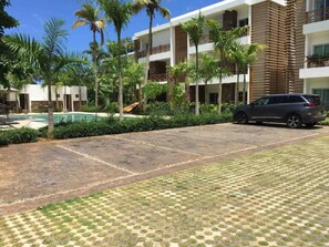 Ein Hotelinnenhof mit Swimmingpool, Palmen und einem am Rand geparkten Auto.