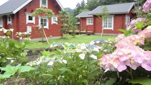 A red wooden house with a sloped roof, surrounded by a garden with hydrangea flowers. - Yufuin Onsen Cottage Kohan (Yufu)
