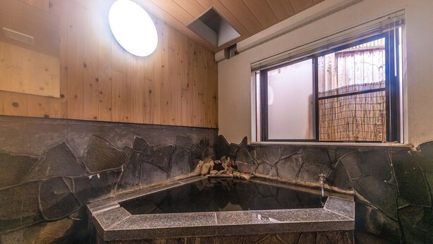 A stone hot tub in a room with wooden walls and a window. - Yufuin Onsen Cottage Kohan (Yufu)