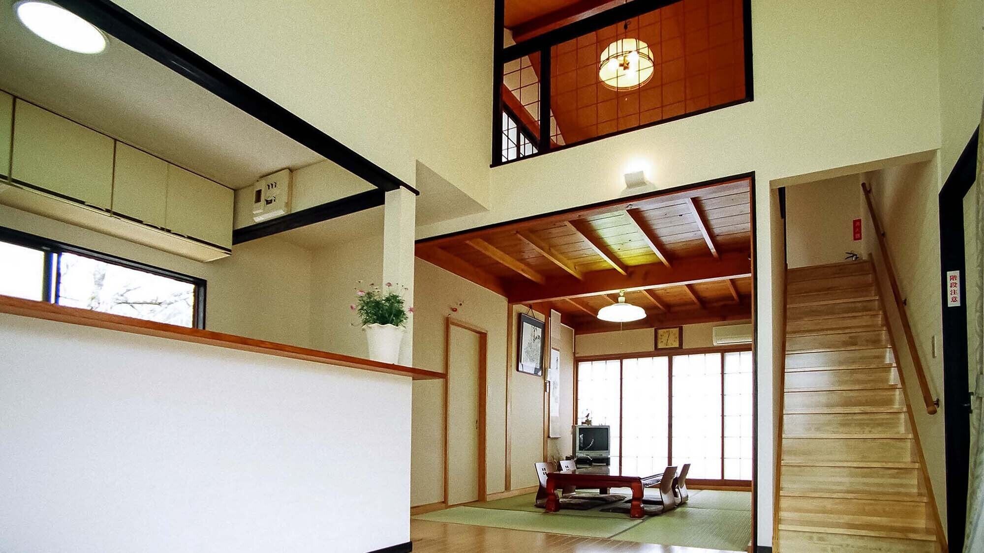 A traditional Japanese interior with tatami flooring, a wooden staircase, and a view of the outside through a sliding door.