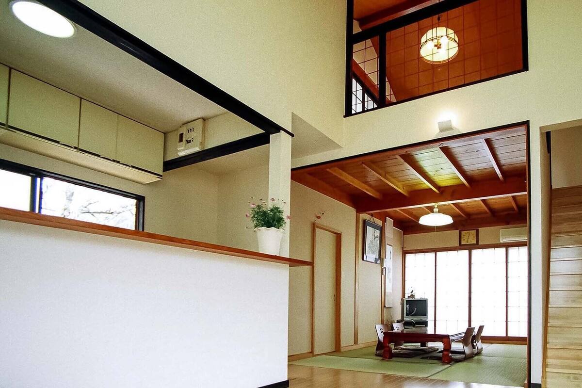 A traditional Japanese interior with tatami flooring, a wooden staircase, and a view of the outside through a sliding door.