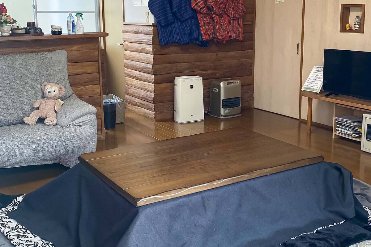 A living room with a sofa, a small table, a TV, a microwave, and a heater.