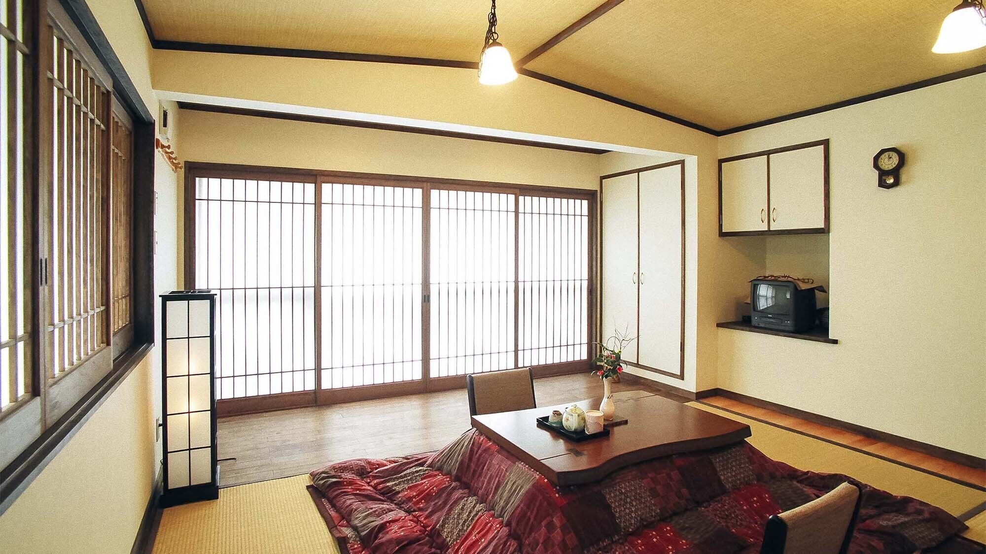Una habitación tradicional japonesa con suelo de tatami, una mesa baja con un juego de té, puertas correderas y un televisor en un estante.