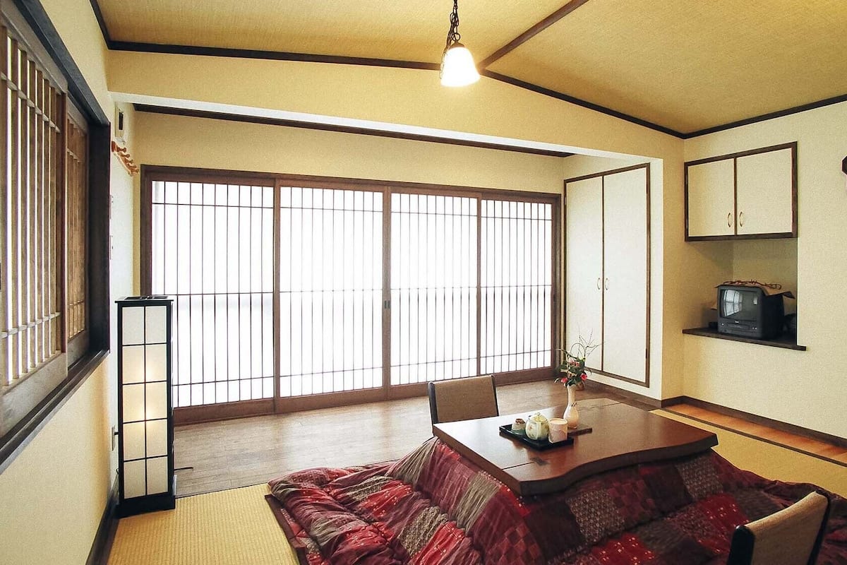 A traditional Japanese room with tatami flooring, a low table with a tea set, sliding doors, and a television on a shelf.