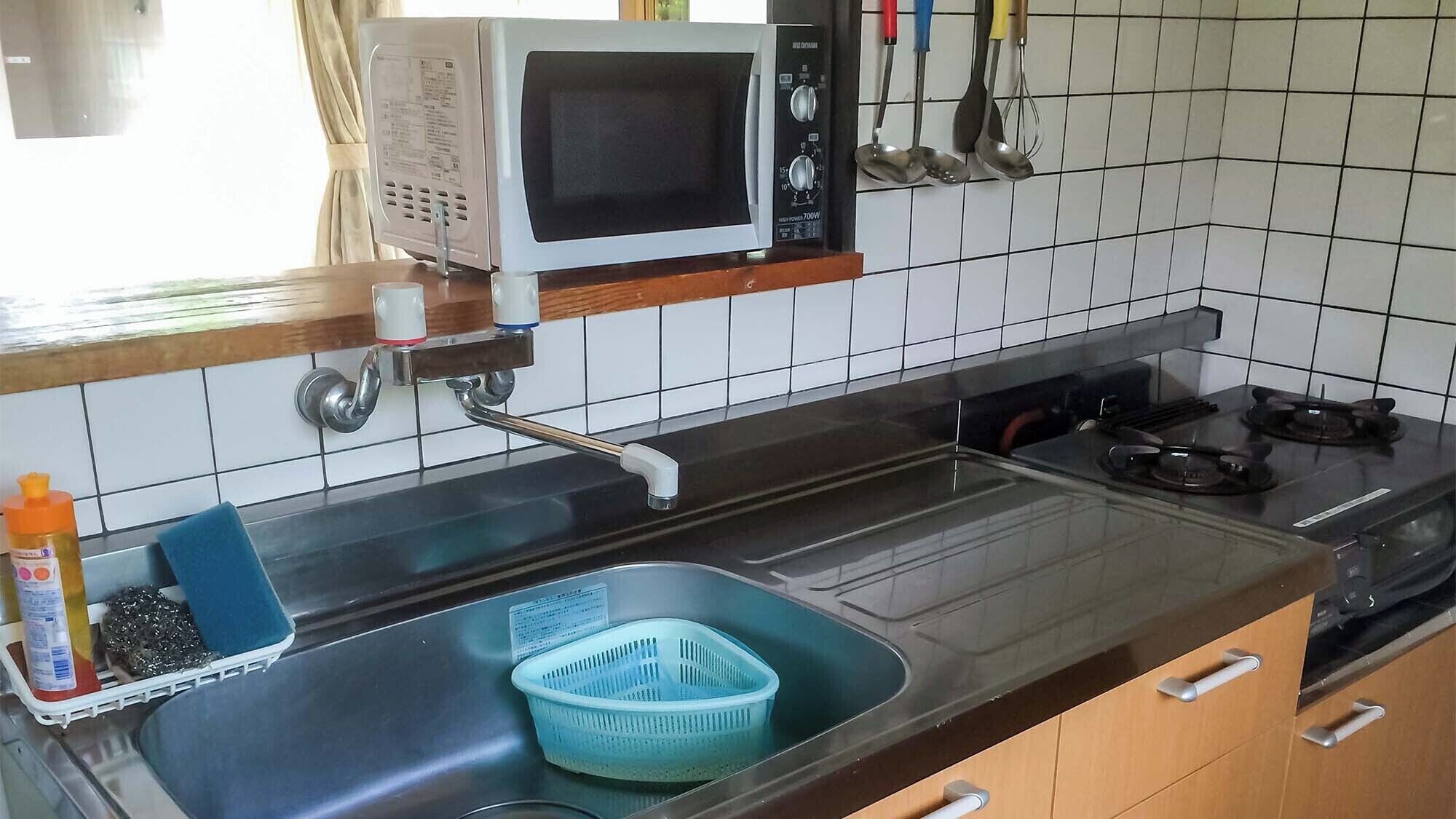 A kitchen with a microwave, sink, stove, and various utensils.