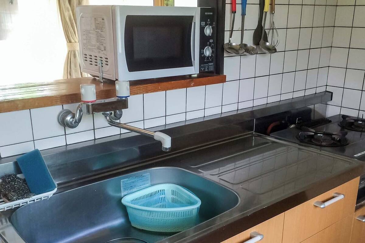A kitchen with a microwave, sink, stove, and various utensils.