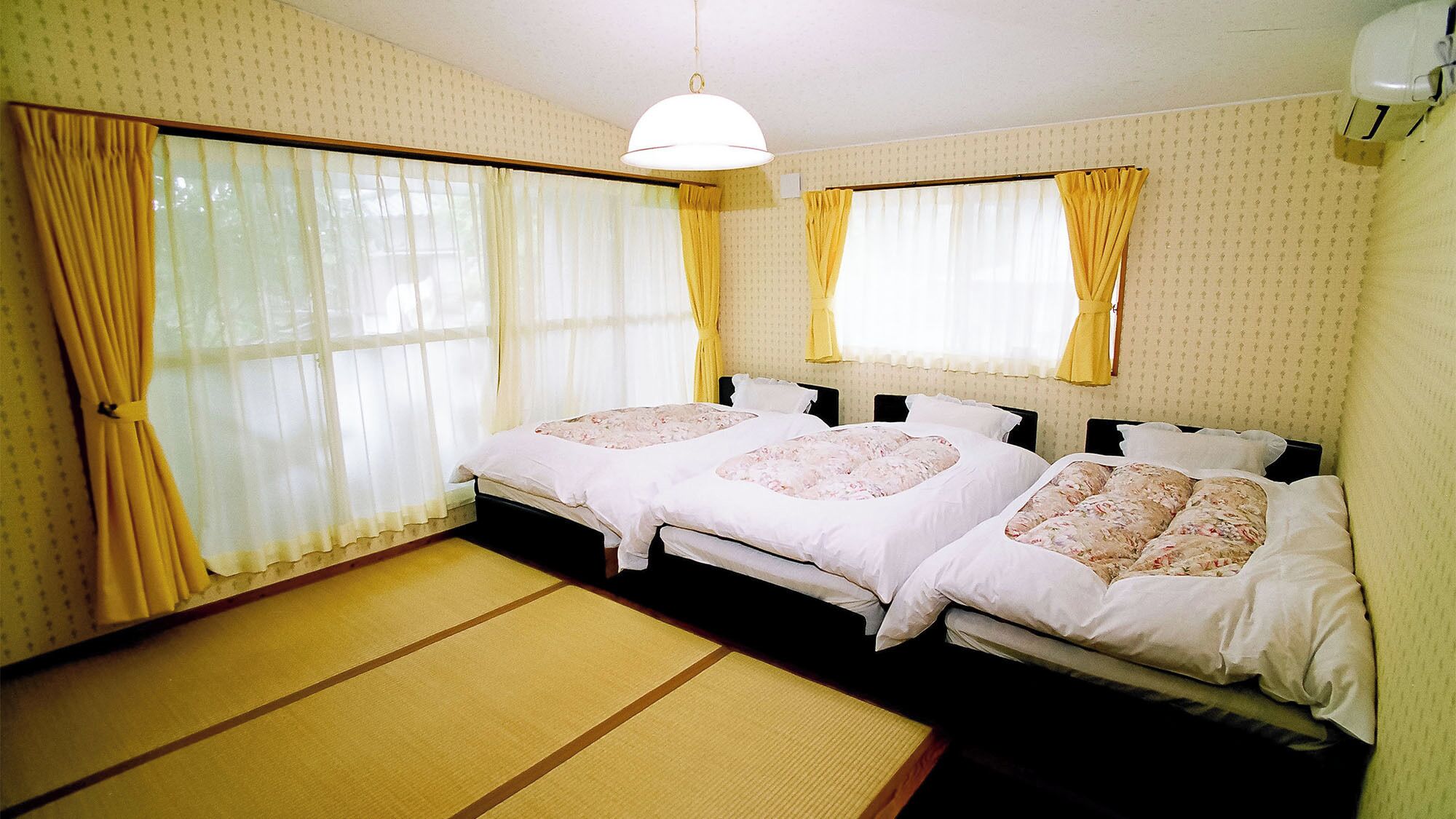 A room with two beds, a tatami mat floor, and a hanging light fixture.