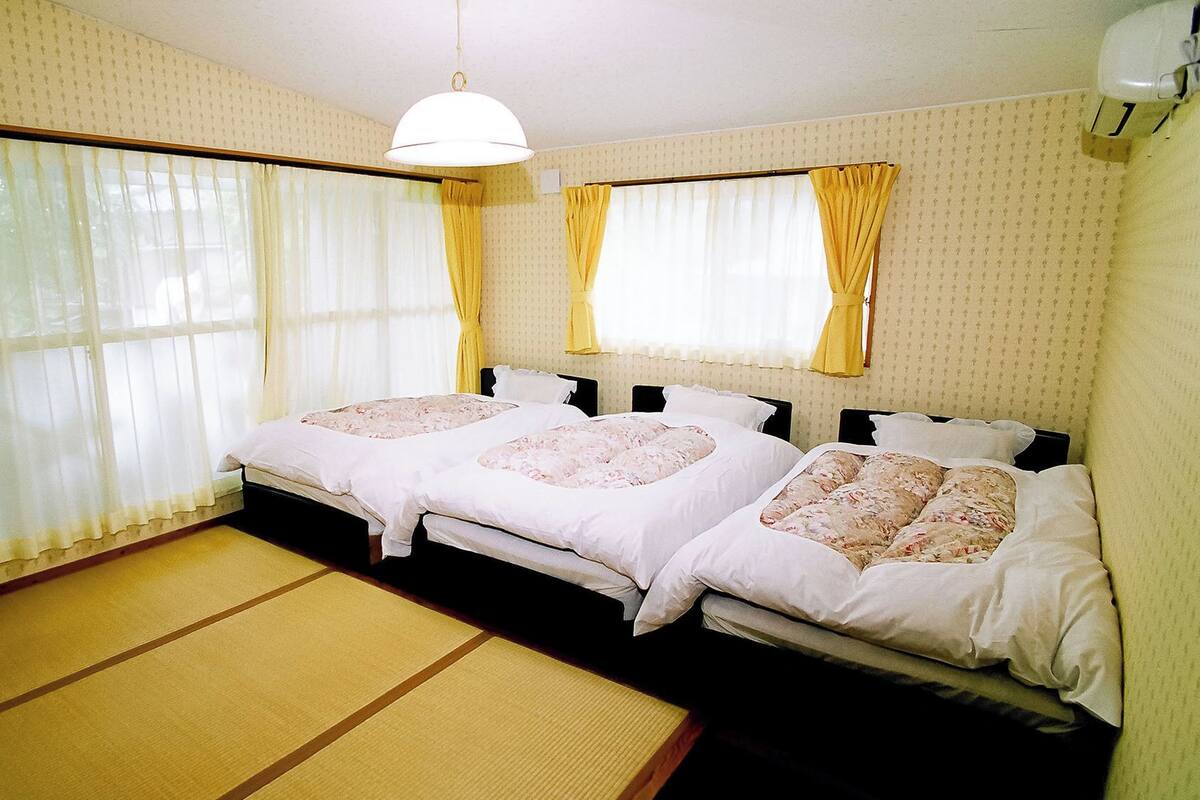 A room with two beds, a tatami mat floor, and a hanging light fixture.