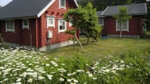 A red house with a sloped roof, a small porch, and a garden with white flowers. - Yufuin Onsen Cottage Kohan (Yufu)