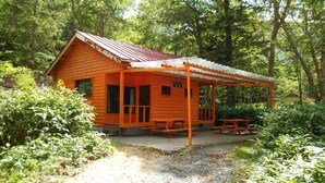 A small wooden cabin with a red roof, a covered porch, and a picnic table.