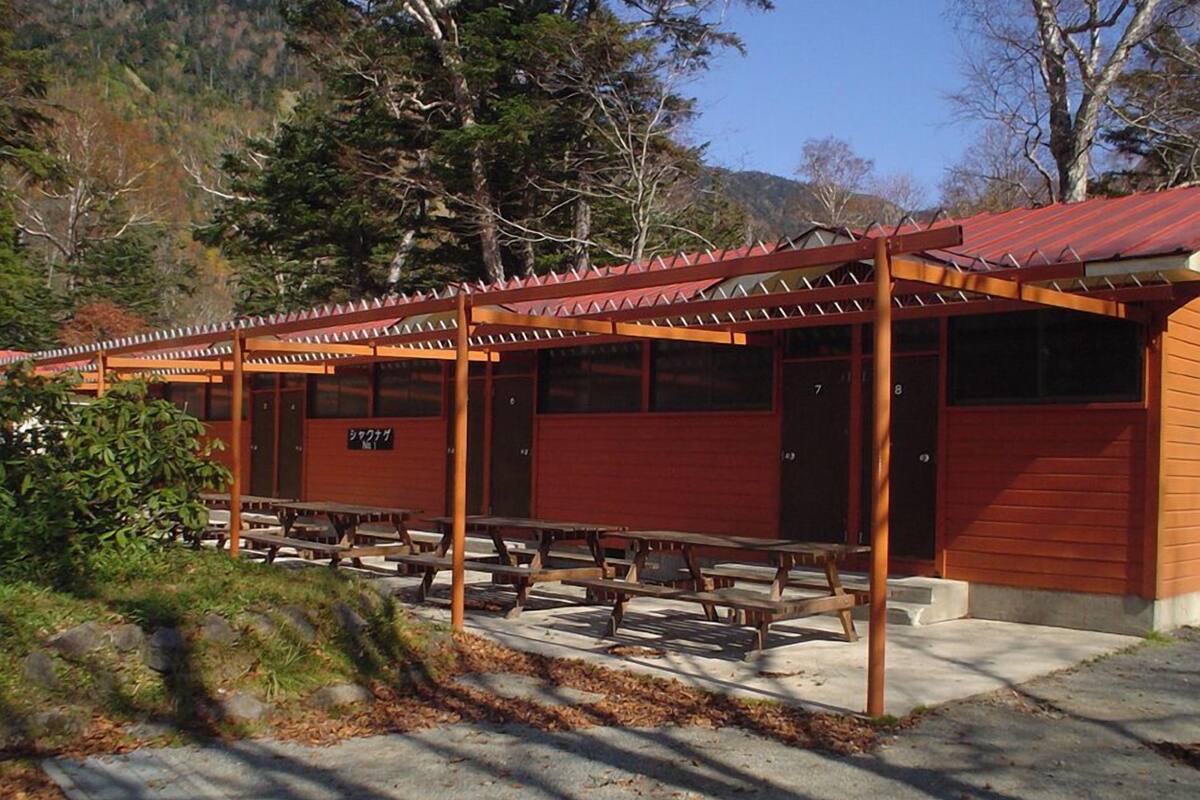 Een overdekt terras met picknicktafels, een houten pergola en een gebouw met een rood dak.