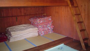 A wooden room with a bunk bed, a stack of folded blankets, and a ladder.