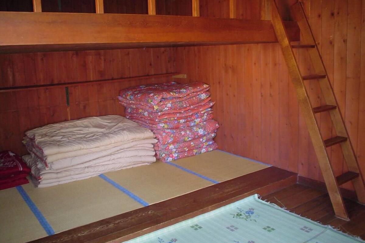Een houten kamer met een stapelbed, een stapel opgevouwen dekens en een ladder.