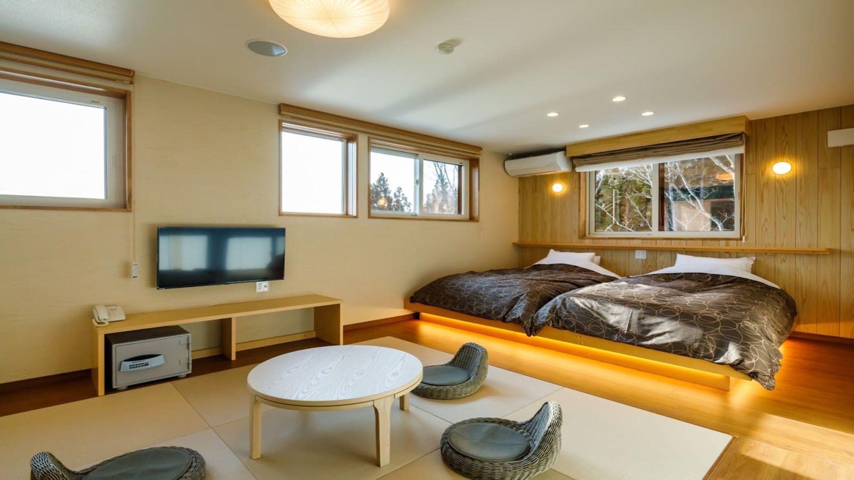 Una camera da letto moderna con un letto grande, una TV, una scrivania e una finestra vista alberi.