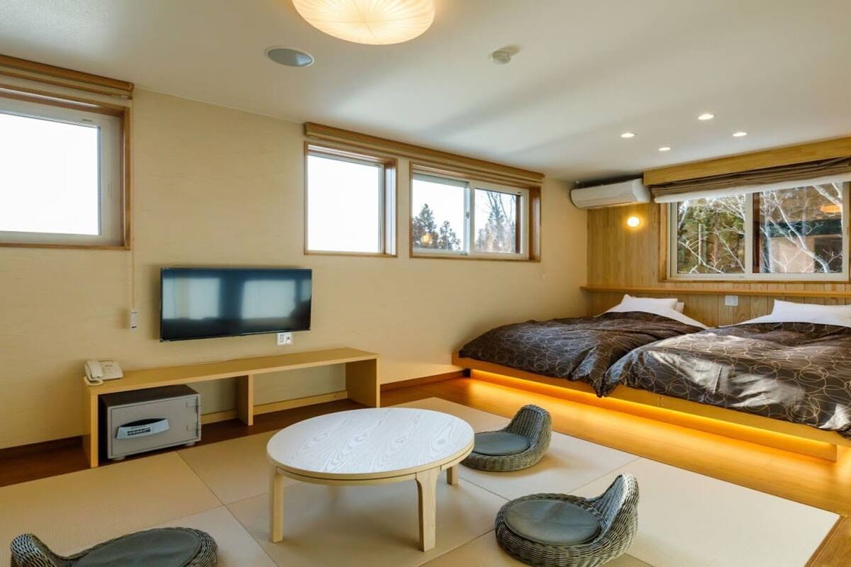 Une chambre moderne avec un grand lit, une télévision, un bureau et une fenêtre donnant sur des arbres.