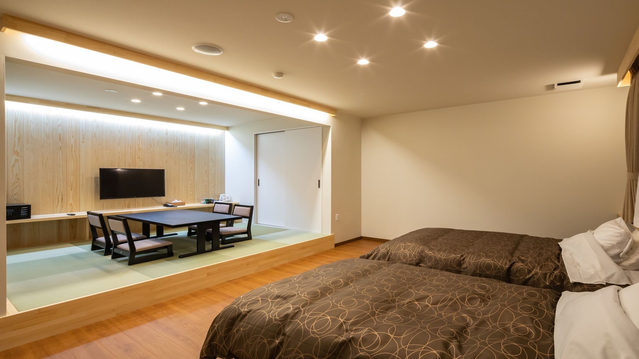 Una camera d'albergo con un letto, una scrivania con una sedia, una televisione e una porta scorrevole.