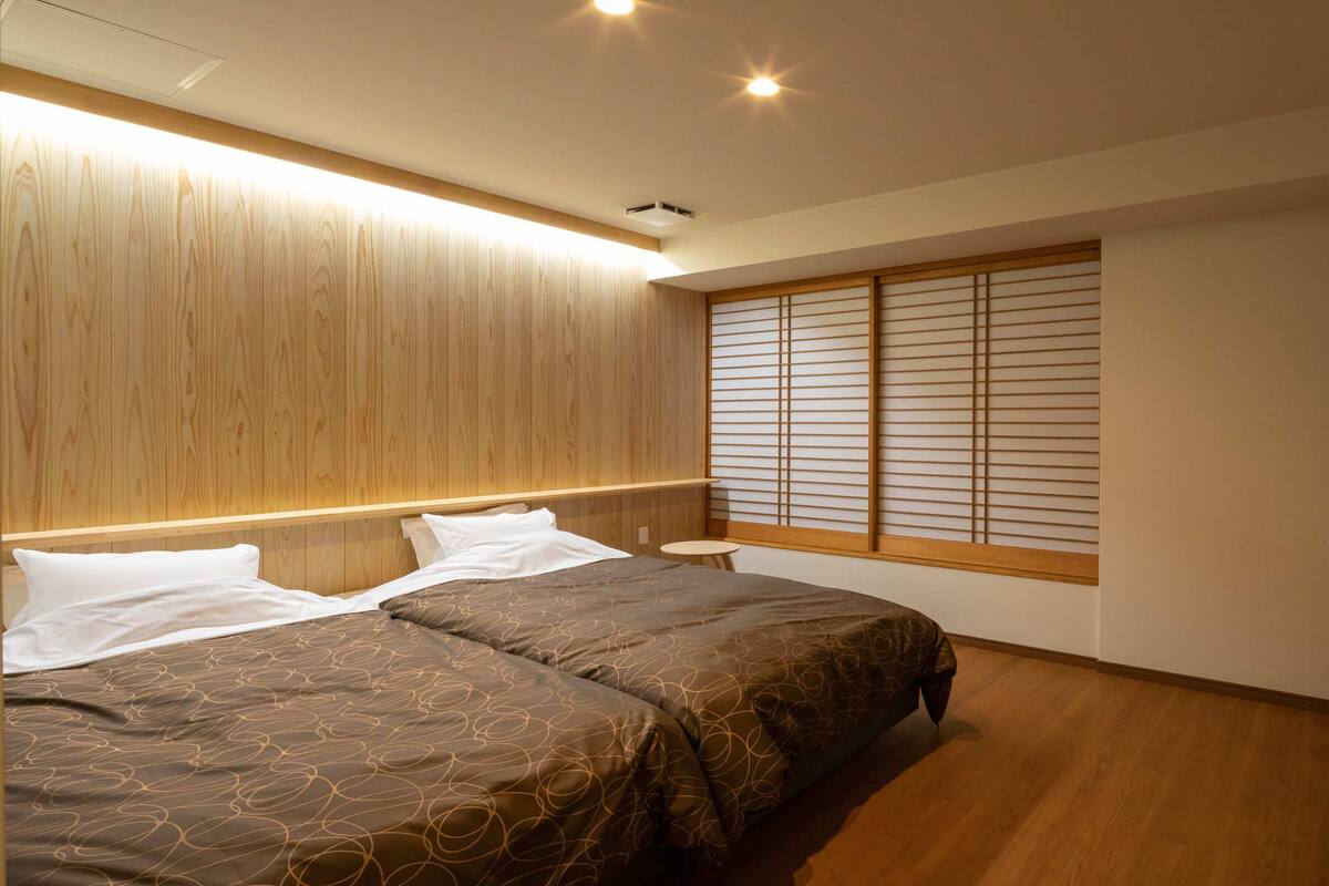 Une chambre à coucher avec un lit, des tables de chevet, une fenêtre avec des panneaux coulissants de style japonais (shoji) et un plafond en bois.