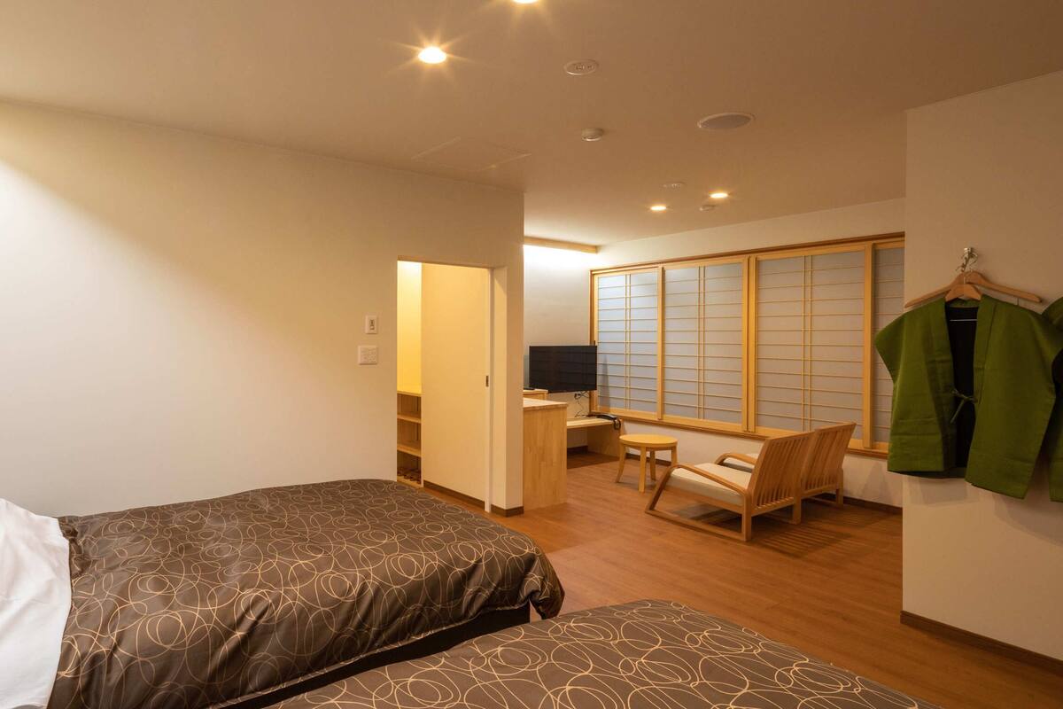 Une chambre d’hôtel avec deux lits, un bureau, une chaise et une porte coulissante traditionnelle.
