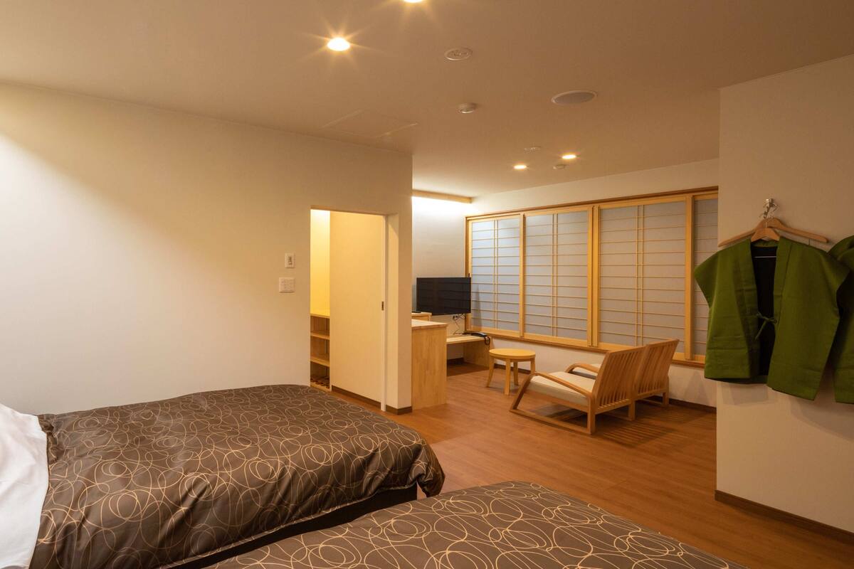 Une chambre d’hôtel avec deux lits, un bureau, une chaise et une porte coulissante traditionnelle.