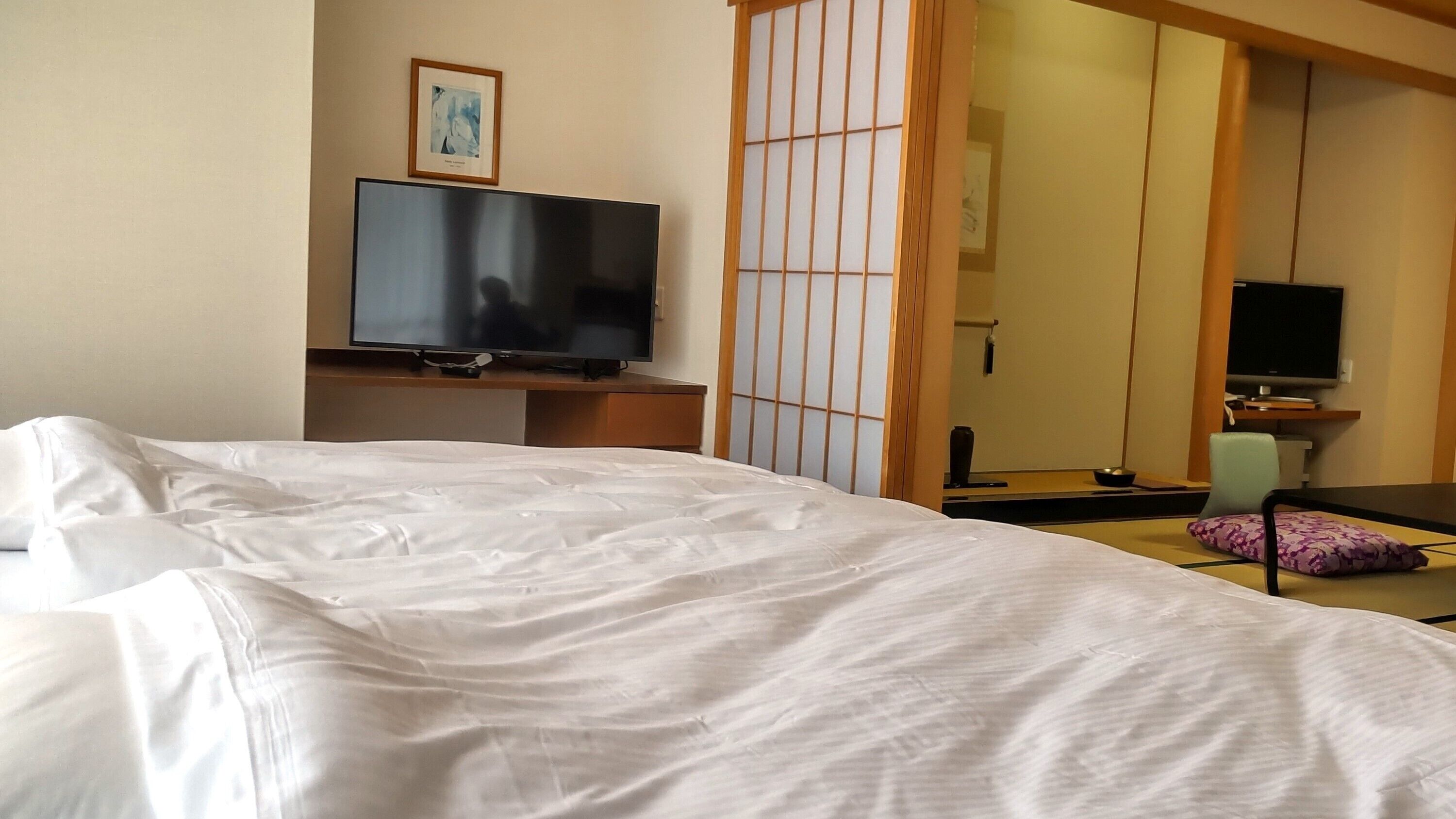 A hotel room with a bed, a television on a stand, a chair, and a mirror.