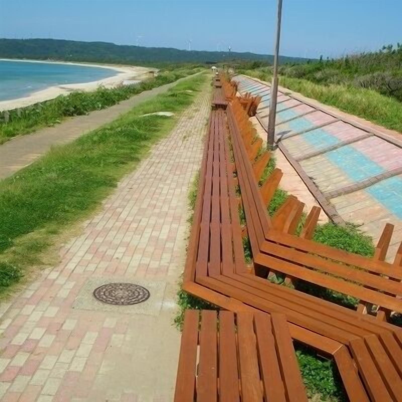 A wooden pathway leading to a beach with a clear view of the ocean and distant hills.