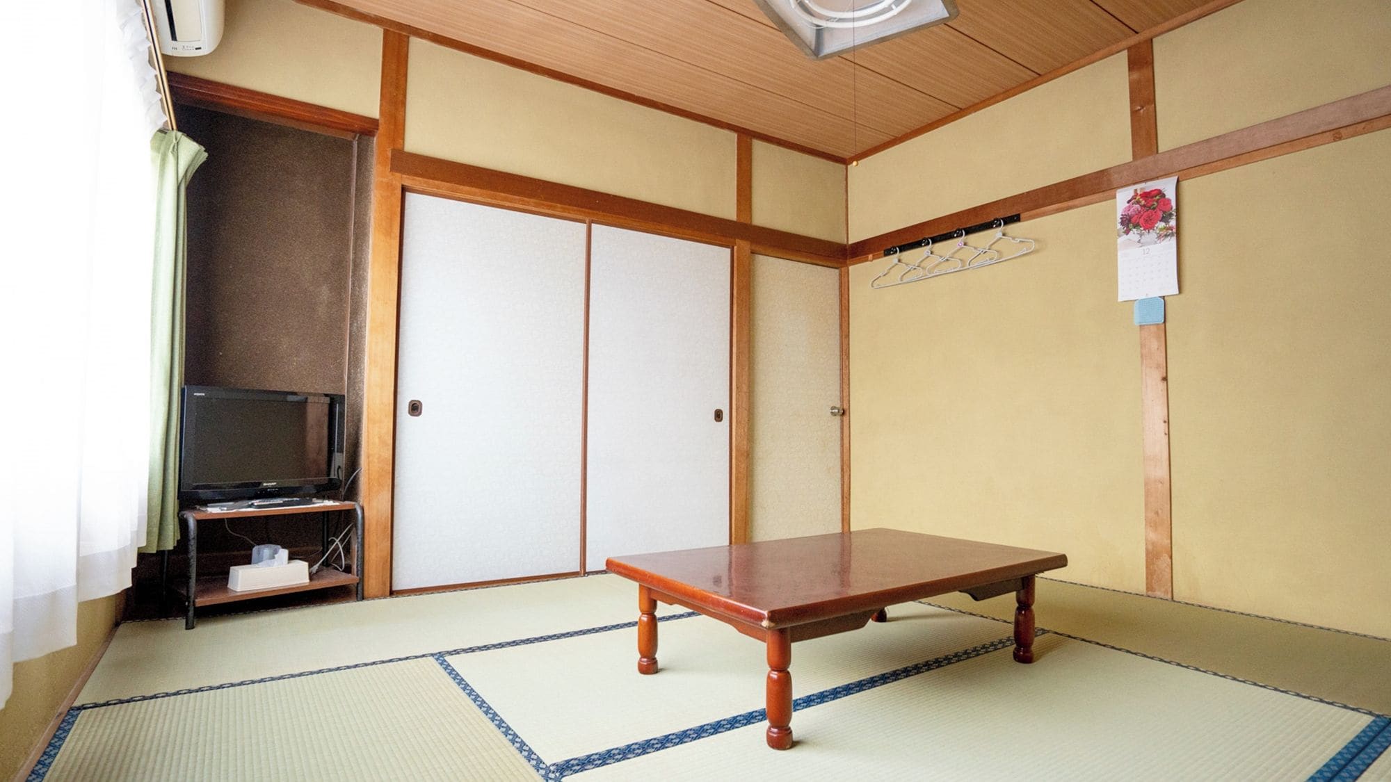 A traditional Japanese room with tatami flooring, a low wooden table, a television on a stand, and sliding doors.