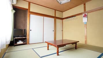 A traditional Japanese room with tatami flooring, a low wooden table, a television on a stand, and sliding doors.