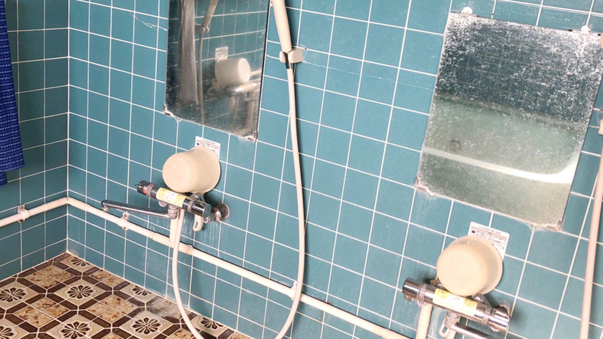 A bathroom with blue tiled walls, two toilets, and visible plumbing fixtures.