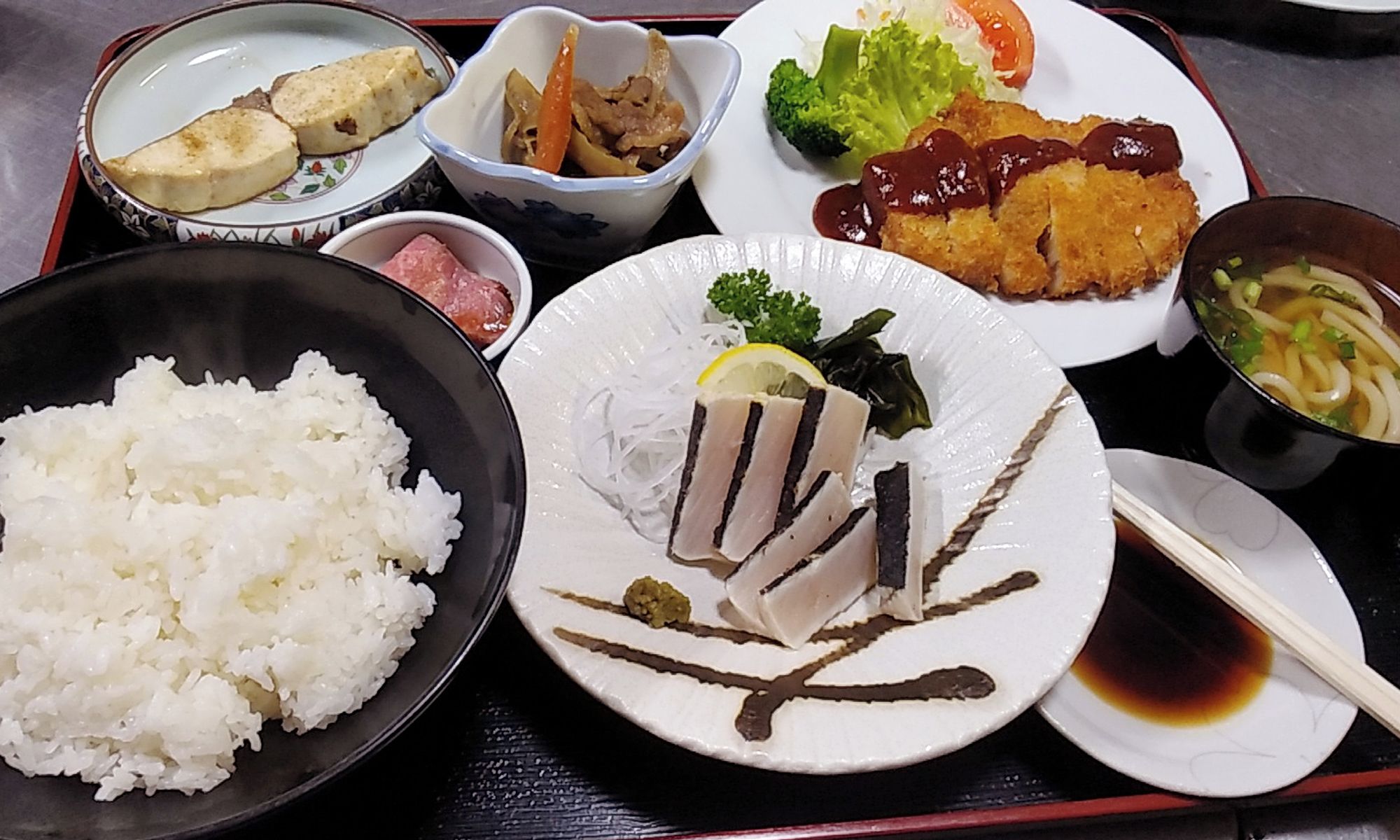 Een dienblad met diverse gerechten, waaronder rijst, sashimi, tempura en een kom soep.