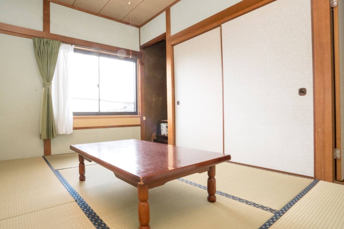 A traditional Japanese room with tatami flooring, a wooden table, a sliding door, and a window with curtains.