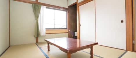 A traditional Japanese room with tatami flooring, a wooden table, a sliding door, and a window with curtains.
