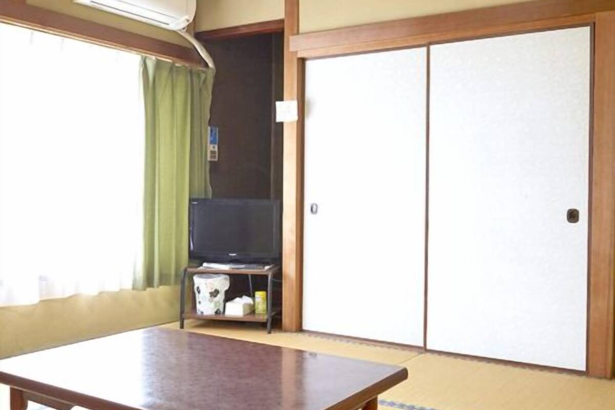 A room with tatami flooring, a wooden table, a television on a stand, and sliding doors.