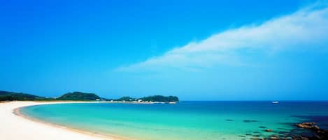 A beach with clear turquoise water, a sandy shore, and a small island in the distance.