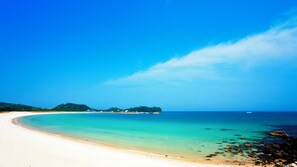 Una playa con agua turquesa cristalina, una orilla arenosa y una pequeña isla en la distancia.