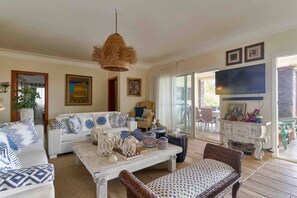 A living room with a white sofa, a wicker chair, a coffee table with decorative items, and a television on the wall. - ®3BR{Beach~Essence}@Terrenas +Pool+Maid+Beachfront (Las Terrenas)