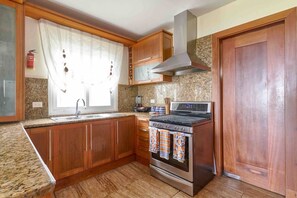 A kitchen with wooden cabinets, a stainless steel stove, a microwave, and a window with curtains. - ®3BR{Beach~Essence}@Terrenas +Pool+Maid+Beachfront (Las Terrenas)