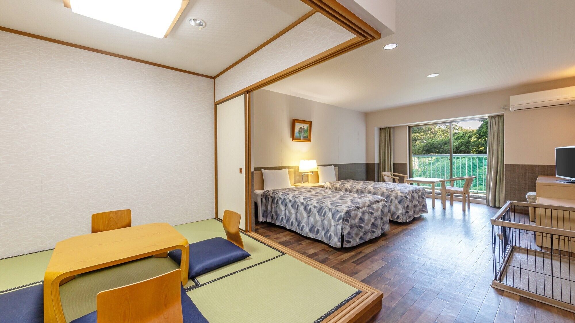 A hotel room with two beds, a dining table, a TV, and a balcony with a view.