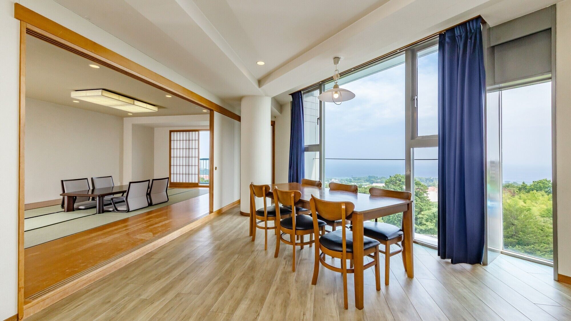 A spacious room with a dining area, large windows, and a view of the outdoors.
