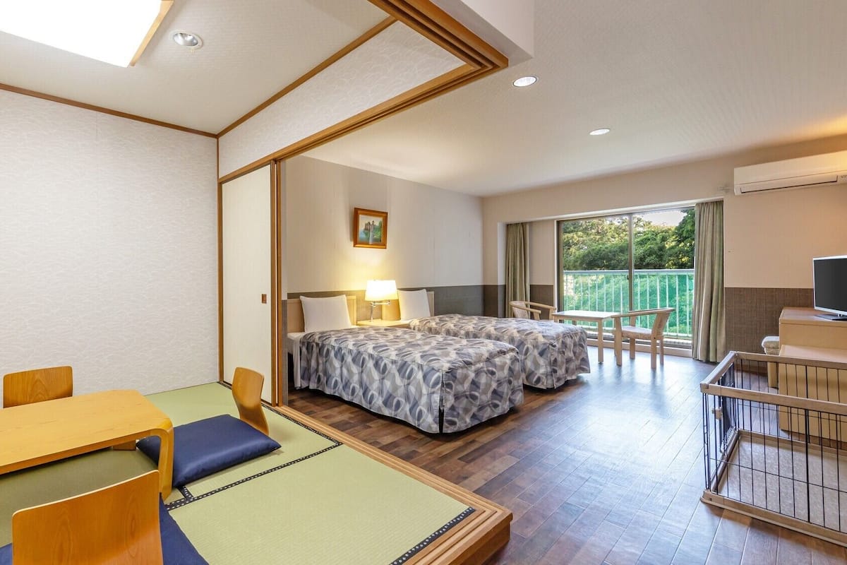 A hotel room with two beds, a dining table, a TV, and a balcony with a view.