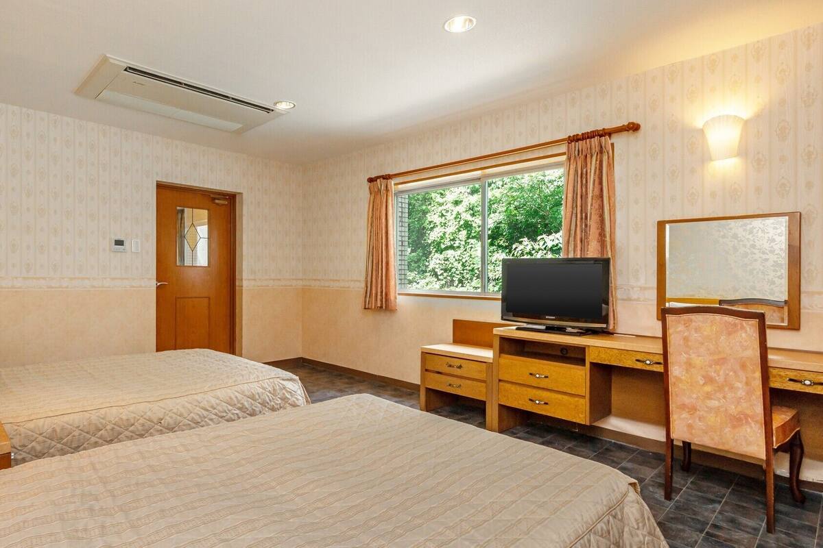 A hotel room with two beds, a desk, a television, a mirror, and a window with curtains.
