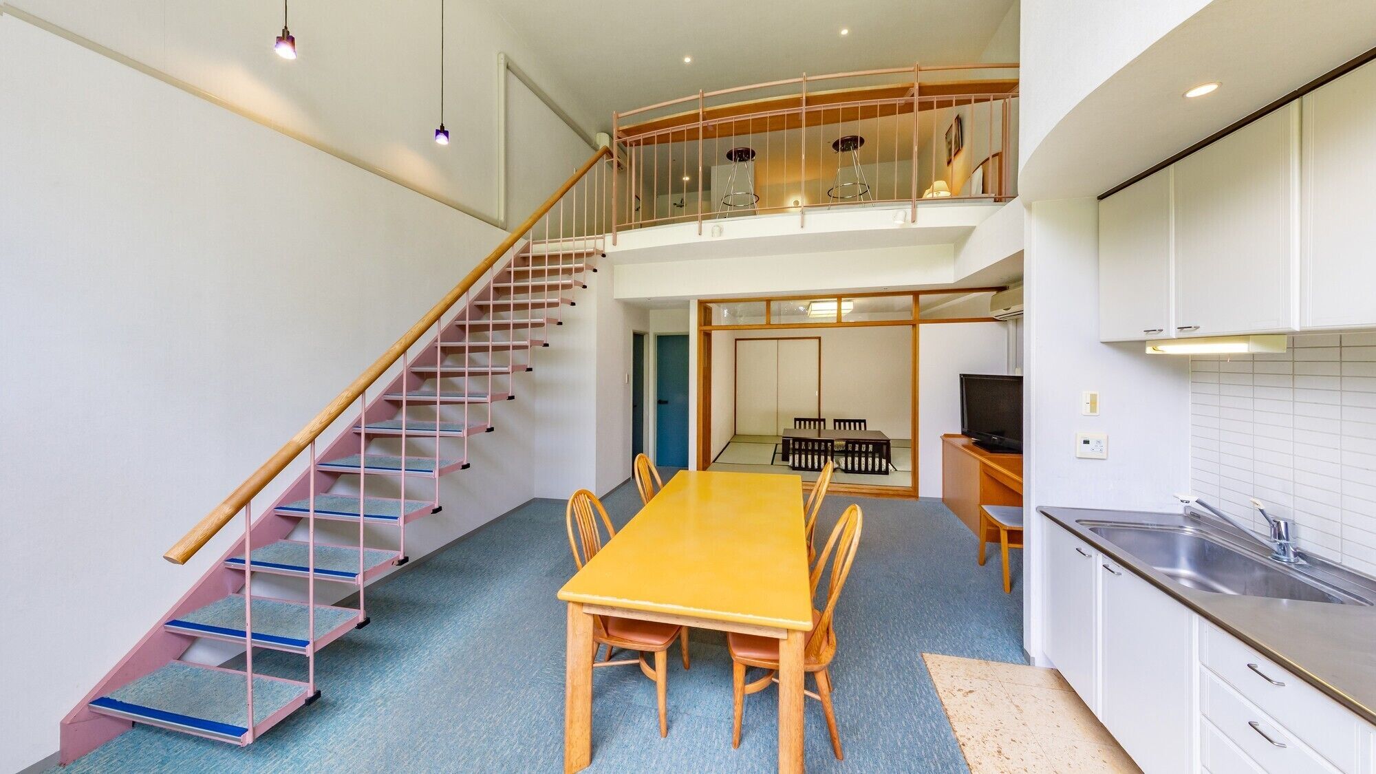 A modern apartment with a dining area, kitchen, and a staircase leading to a loft.