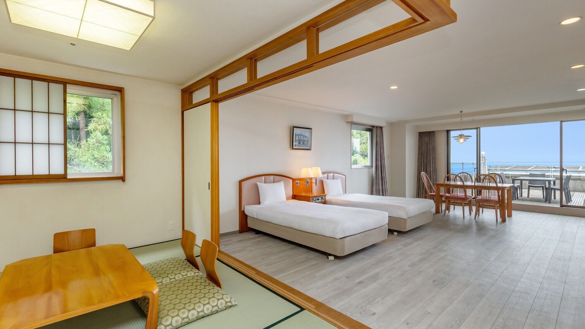 A hotel room with two beds, a dining area, and a balcony with a view.