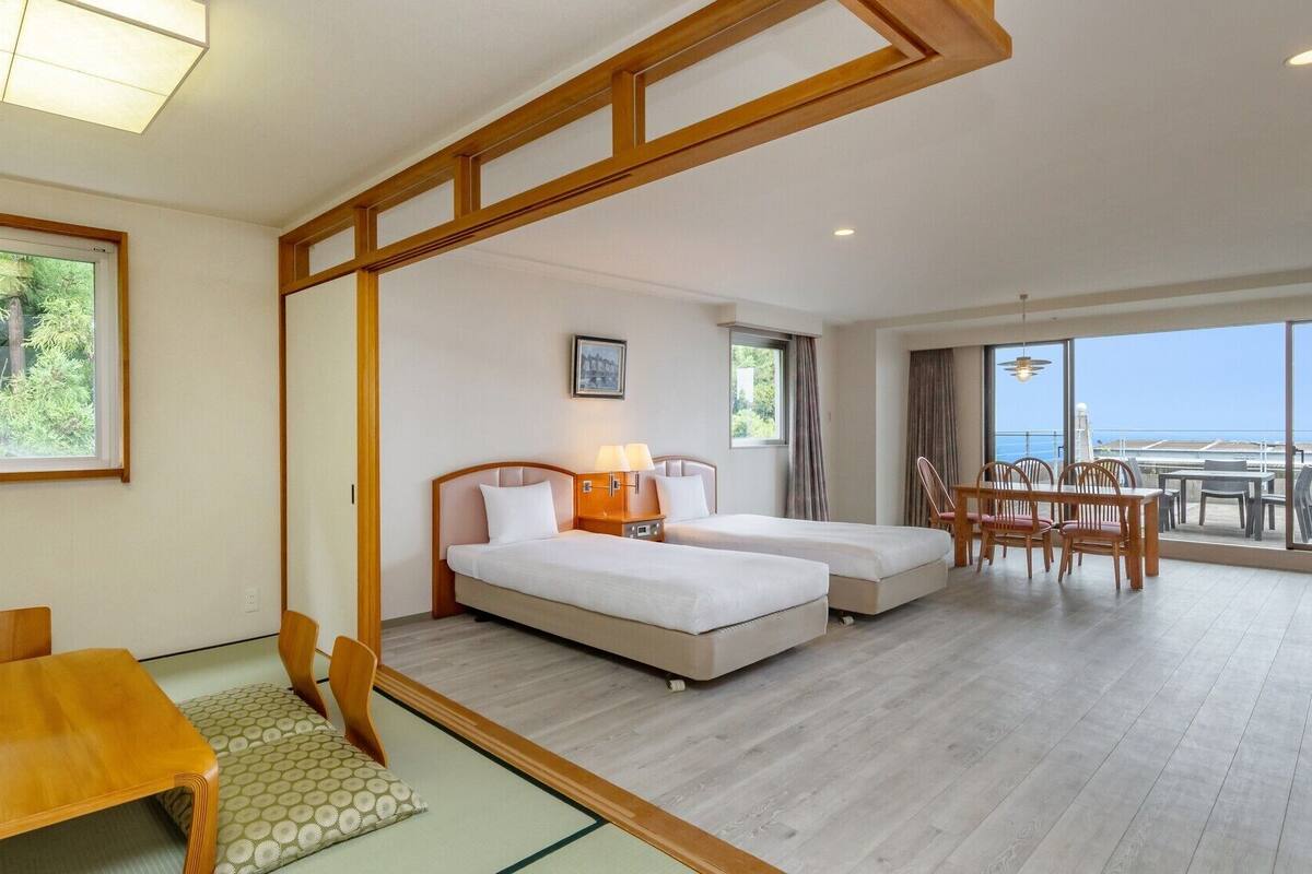 A hotel room with two beds, a dining area, and a balcony with a view.