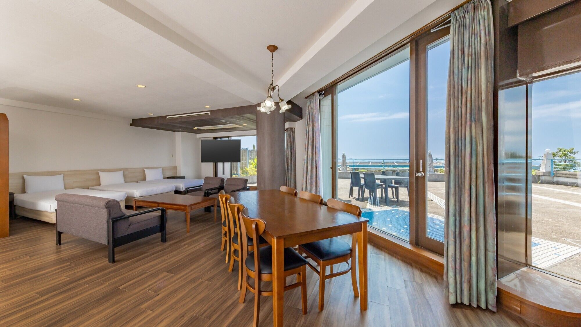 A modern hotel room with a dining area, sofa, and large windows offering a view.